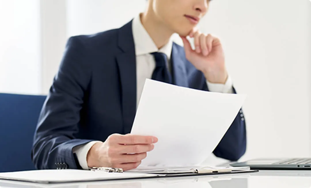 考えながら書類を確認する男性の画像